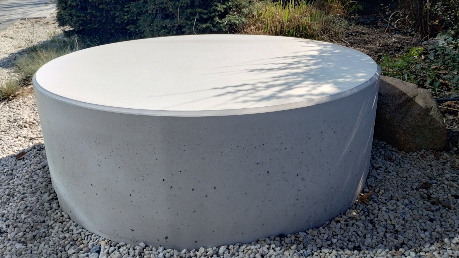 Betonowy Stolik Giro ustawiony na kruszywie, wśród ogrodowej zieleni