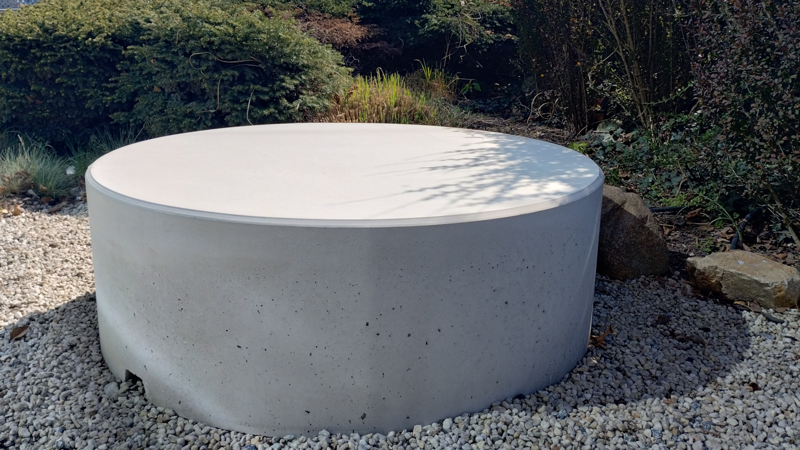 Betonowy Stolik Giro ustawiony na kruszywie, wśród ogrodowej zieleni