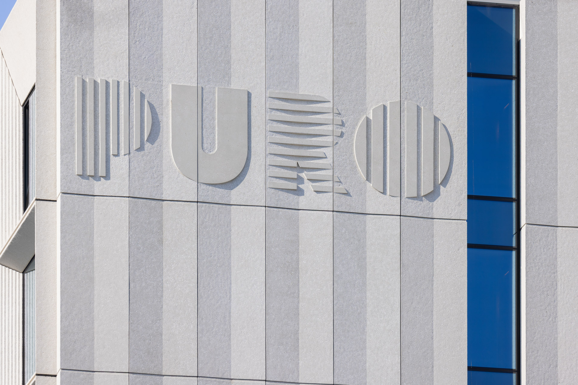 Logo hotelu PURO osadzone w prefabrykowanych panelach elewacyjnych – przykład integracji funkcji estetycznych i informacyjnych w betonie architektonicznym.
